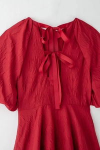 Détail de la robe rouge avec dos nu à nœud papillon et texture de manches bouffantes