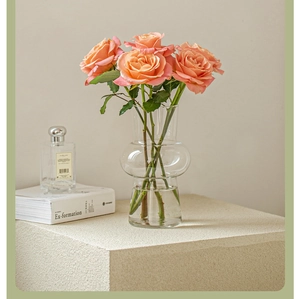 Detail of a transparent glass vase holding pink roses next to an Ex-formation book