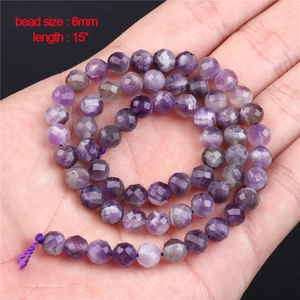 Close-up of 6mm faceted natural amethyst round beads held by hand for jewelry making