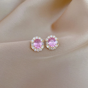 Macro view of pink oval zircon earrings with halo diamond setting on gold metal base