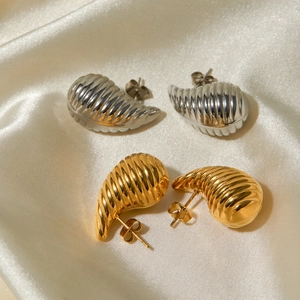 Macro shot of gold and silver textured croissant dome earrings on beige silk fabric
