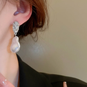 Detail of silver textured earrings with baroque pearls worn on model with black blazer