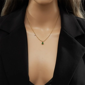 Close-up of a gold chain necklace with a green waterdrop pendant worn on a black blazer