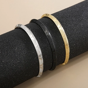 Detailed close-up of three C-shaped titanium steel bracelets in silver, gold, and black
