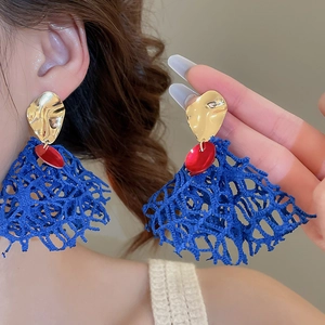 Detailed view of blue fabric tassel earrings with gold metal stud and red accents