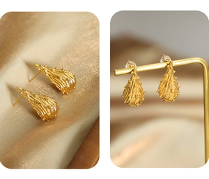 Detail van onregelmatige gouden druppeloorbellen op zijde en een metalen displaystandaard