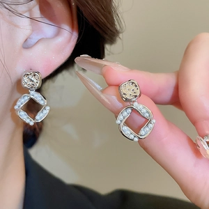 Detailed view of silver square twisted earrings with embedded pearls worn on ear