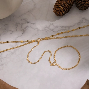 Detailed view of gold layered zircon finger chain on elegant marble surface with pine cone