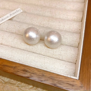 Dettaglio di orecchini con perle bianche su espositore in velluto e cornice in legno