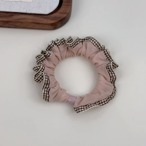 Close-up of a pink fabric scrunchie featuring brown and white plaid ruffled lace edges