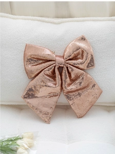 Macro detail of large rose gold sequin bow decoration on soft white wool texture fabric