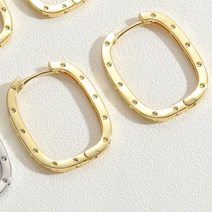 Macro shot of gold-plated rectangular hoop earrings with dotted edge texture and clasp detail