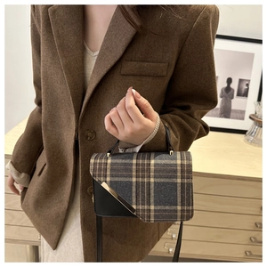 Detailed shot of retro plaid handbag with black leather patchwork and gold metal hardware
