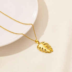 Macro shot of gold-plated monstera leaf pendant with hollow design on fine link chain
