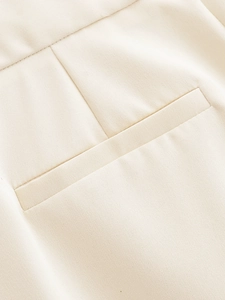 Detail of high waist trousers showing the cream twill fabric and button pocket stitching