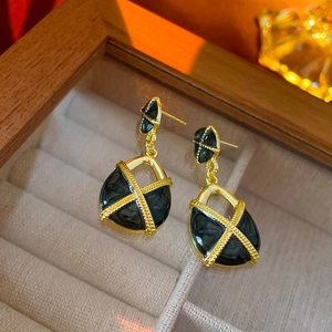 Vue macro de boucles d'oreilles rétro en émail noir avec motif croisé doré sur velours