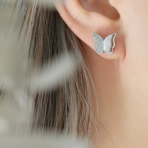 Macro detail of butterfly stud earrings featuring a frosted finish and 3D layered design