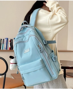 Close-up of light blue durable backpack with a cute white plush puppy charm and logo