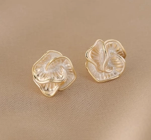 Detail of elegant gold-edged white camellia pearl earrings with textured 3D design