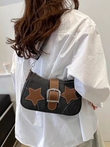Detail of black denim underarm bag featuring brown star patches and silver buckle strap
