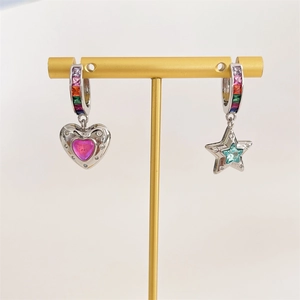 Detail of asymmetric earrings with pink heart and teal star charms on golden display