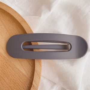 Detail view of a matte grey-purple hollow hair clip on a natural wooden tray and linen
