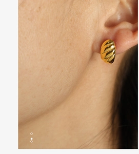 Close-up of a gold croissant style earring with spiral texture on a woman's ear