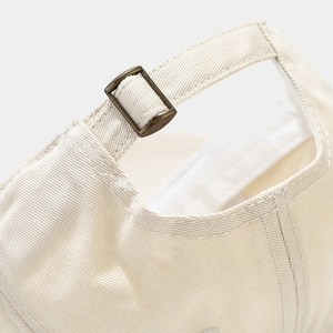 Minimalist cream cotton baseball cap featuring adjustable bronze metal buckle detail