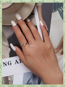 Detail of rose gold hug ring on hand with white nails, next to coffee and magazine
