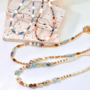 Detail of beaded necklace with freshwater pearls, colorful stones on white silk fabric
