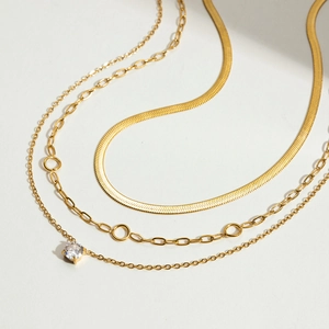 Detailed close-up of triple-layered golden necklace with snake chain and zircon pendant