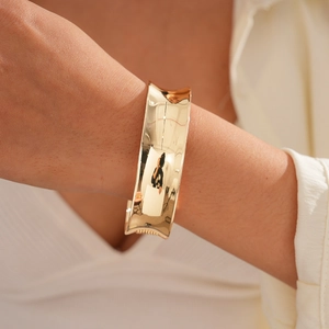 Close-up of polished gold wide open cuff bracelet on a model's wrist with knit background