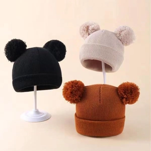 Detail view of kids knit hats with double pom-poms in black, beige and caramel colors