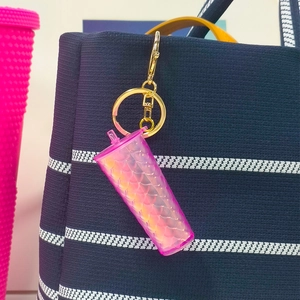 Pink gradient scale texture tumbler keychain hanging on a blue striped handbag