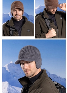 Detail view of winter knit hat with ear flaps and visor on snow mountain background