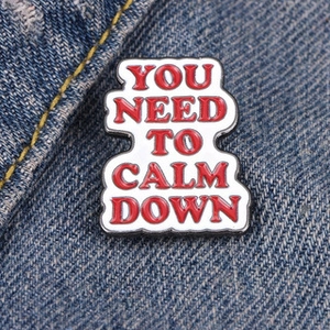 Enamel pin with red You Need To Calm Down text on white background and blue denim