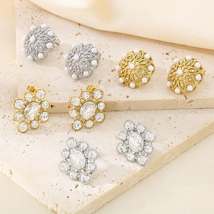 Detailed close-up of crystal and pearl stud earrings displayed on beige stone and silk