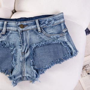 Dettaglio dell'orlo sfrangiato e bottone in metallo su shorts in denim blu elasticizzato