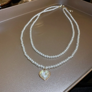 Macro view of double-layer pearl necklace with iridescent opal heart pendant on gold tray