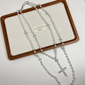 Detail of long pearl necklace with silver cross charms on a wooden display tray