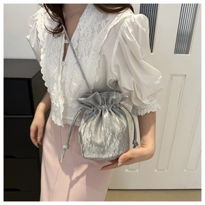 Silver drawstring bucket bag with pleated texture shown on model in home setting