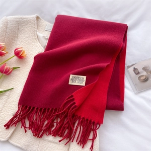Detail of red tassel scarf on white linen featuring stitched designer label and wool texture