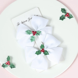 Detail view of two white Christmas hair bows with holly leaf and red berry accents