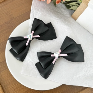 Détail de barrettes nœuds en satin noir avec ruban rose et strass en forme de cœur brillant