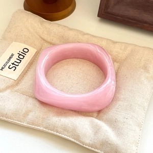 Close-up of pink marbled resin bangle with square structure on soft beige fabric