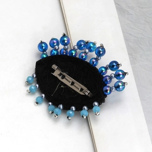 Detailed view of handmade Evil Eye brooch with blue beads on a black fabric base