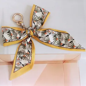 Detail of yellow daisy floral silk bow keychain with golden metal ring for handbags