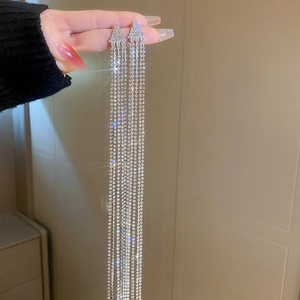 Détail de boucles d'oreilles triangulaires argentées avec élégants longs pompons en strass