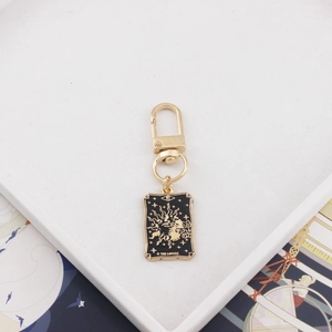 Detail of The Lovers tarot card keychain in black and gold alloy with Roman numeral VI