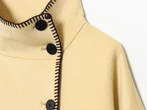 Detail of pale yellow wool coat featuring black buttons and brown contrast stitching